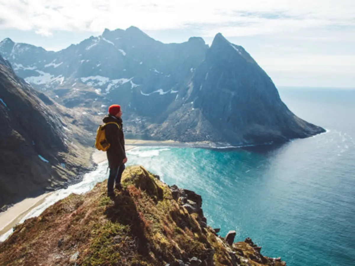 En person står uppe på toppen av ett berg och ser ut över havet och berg i fjärran.